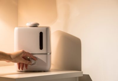 Female hand turn on aroma oil diffuser on the bedside table at n